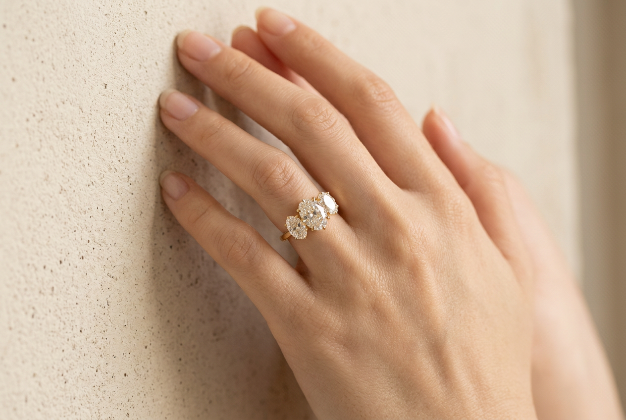 The oval three stone diamond ring worn on a woman's wedding finger against cream concrete