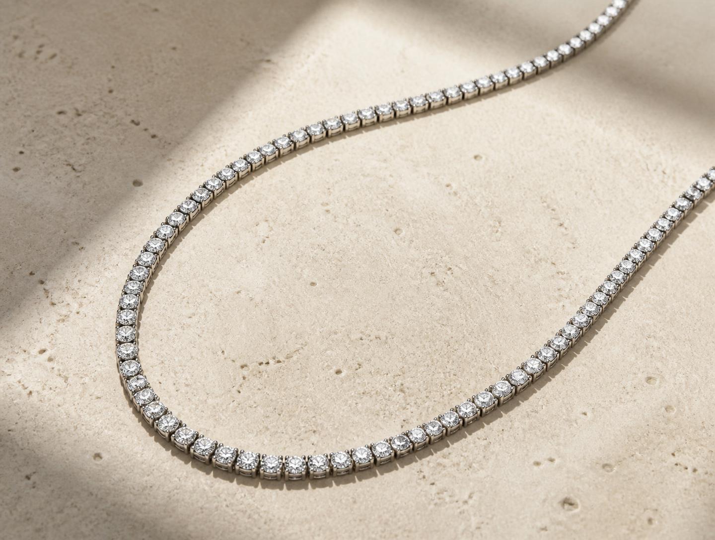 RW The Line 2mm round brilliant diamond tennis necklace in 10k White Gold, resting on a warm cream concrete slab